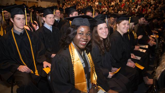 Students in cap and gown sit and smile at the camera during an Honors Graduation ceremony.