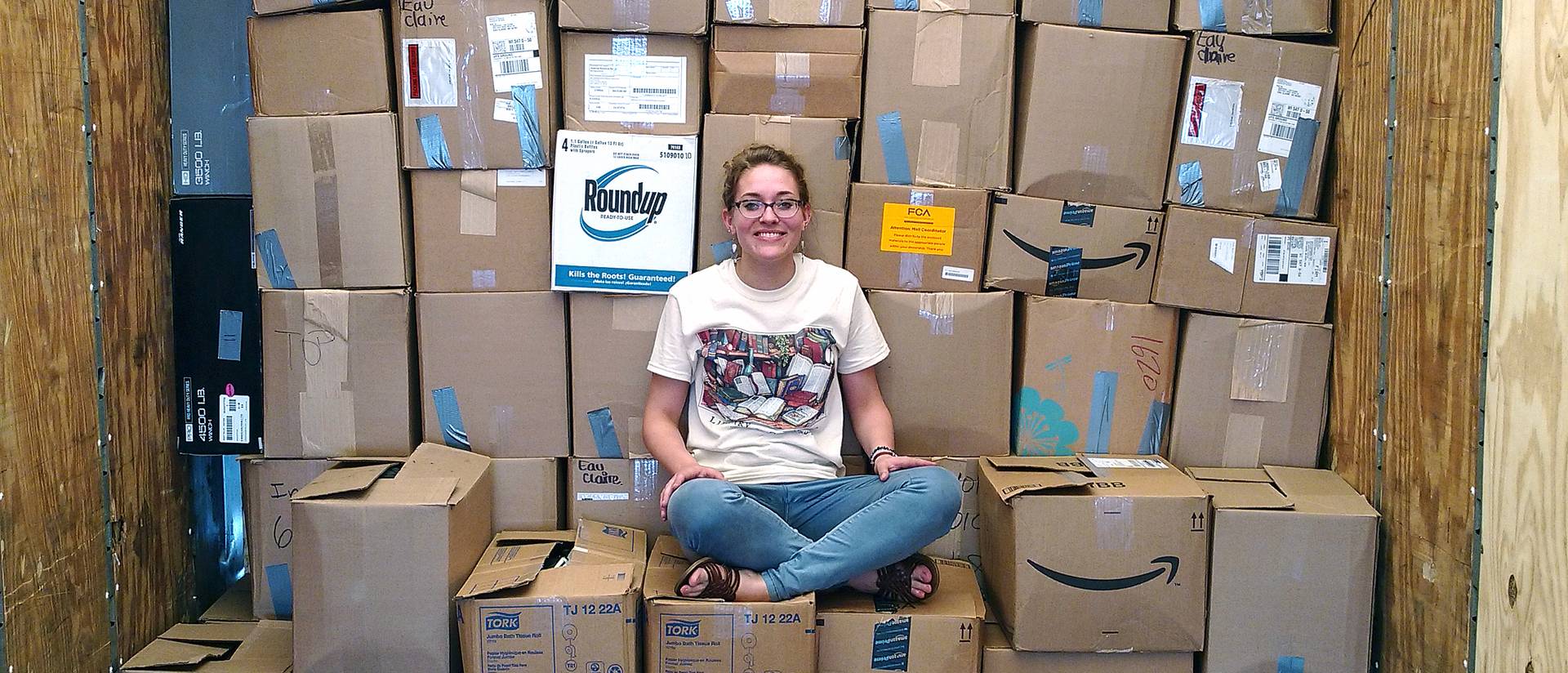 Jenna Vande Zande sits atop boxes containing shoes and smiles.