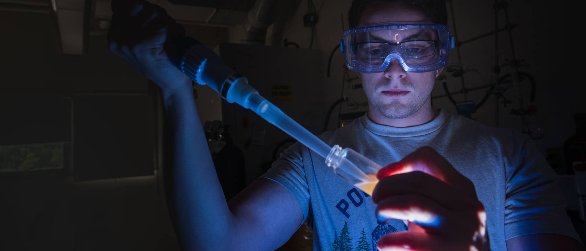 Erik Engness uses a device to place a liquid into a glass container in a dark lab.