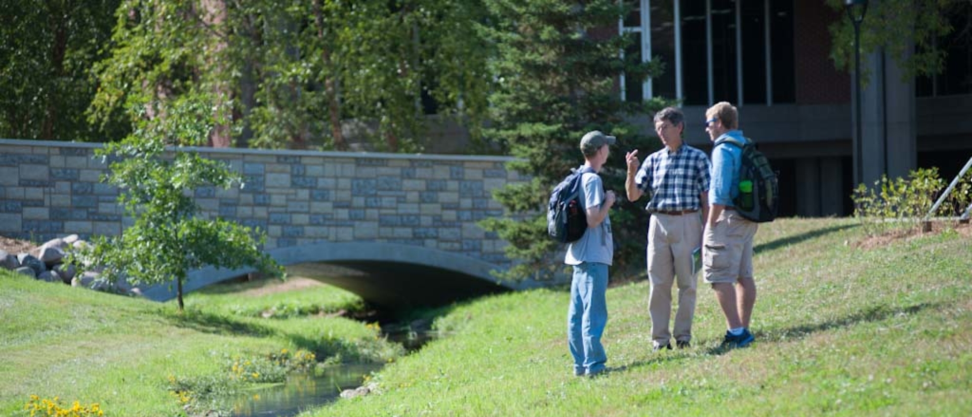 Students and a professor chat by a creek.
