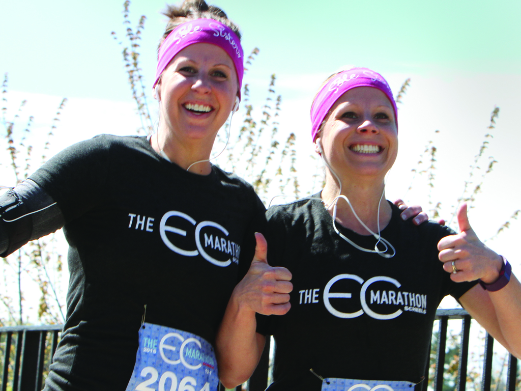 Two young women smiling with a thumbs up as they run the Eau Claire Marathon.