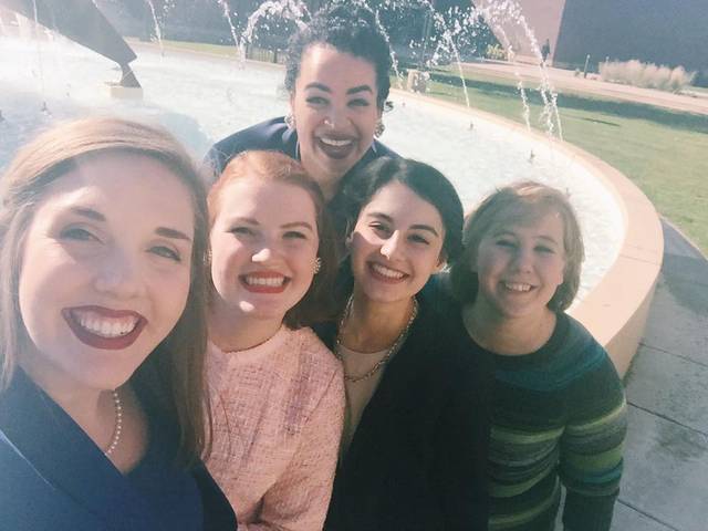 Five people smile while taking a selfie in front of a fountain.