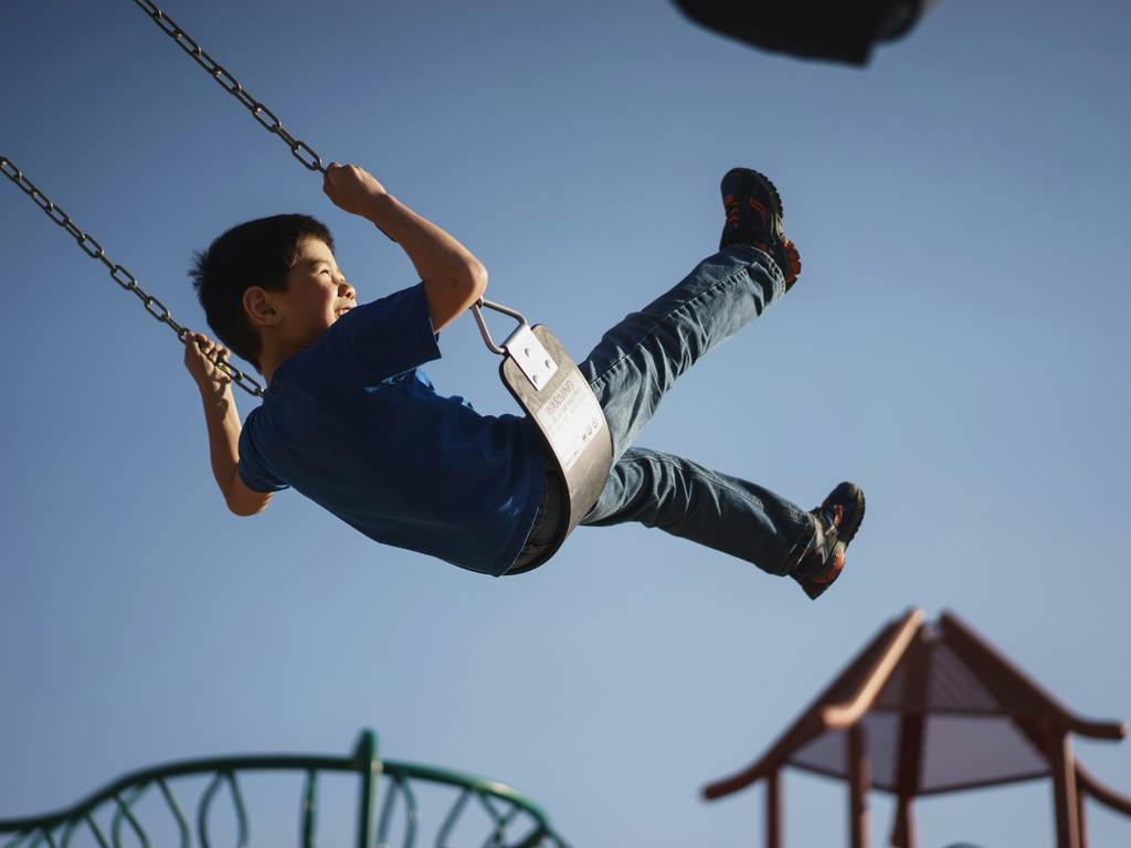 A young boy swings on a swing at a park.