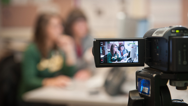 A video camera zoomed in on a professor helping a student.