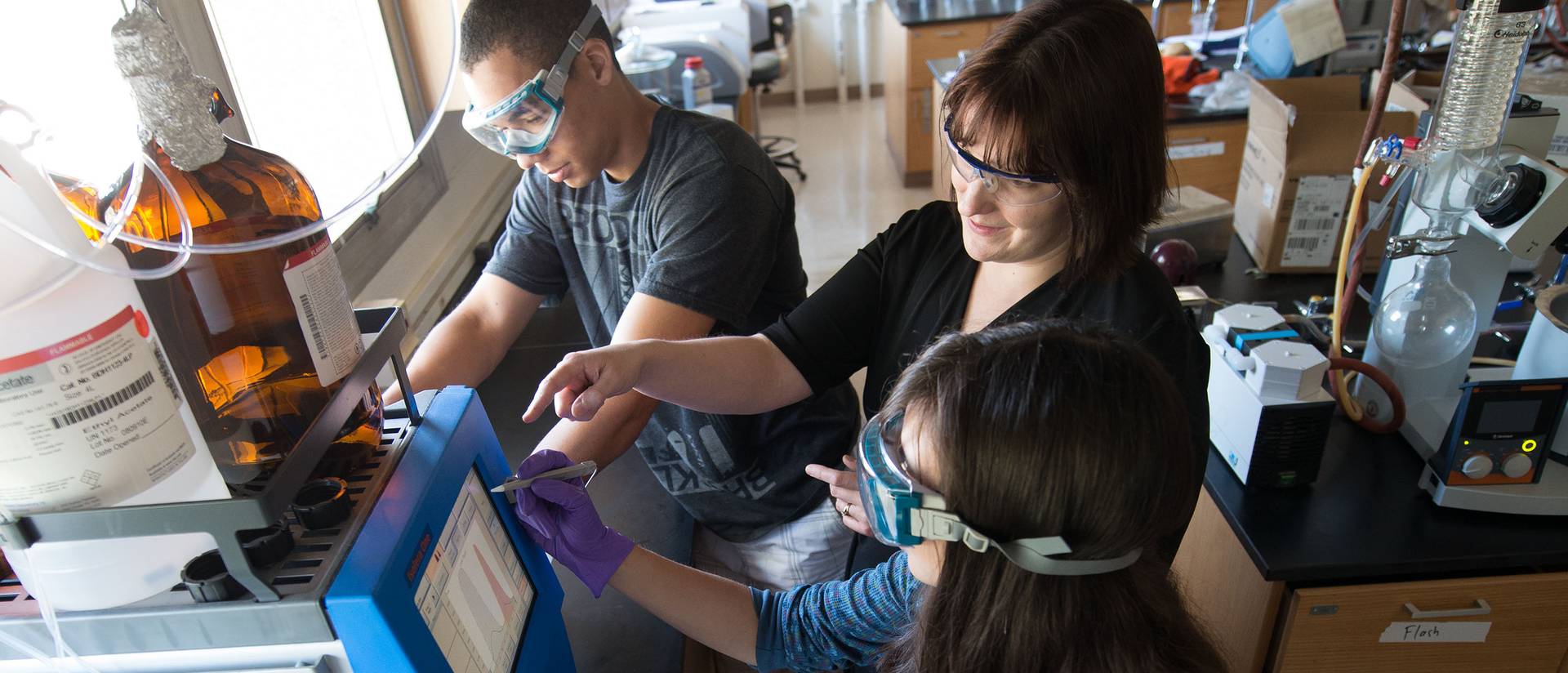 Three people work with laboratory equipment.