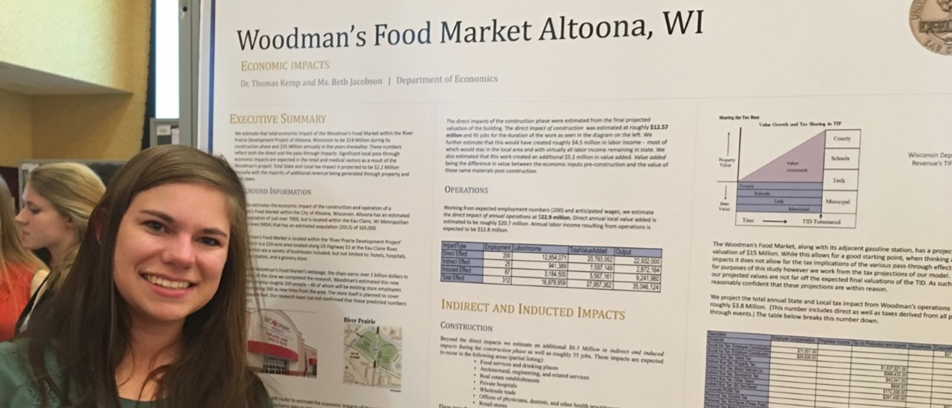 A student smiles next to a board detailing Woodman's Food Market in Altoona during CERCA.