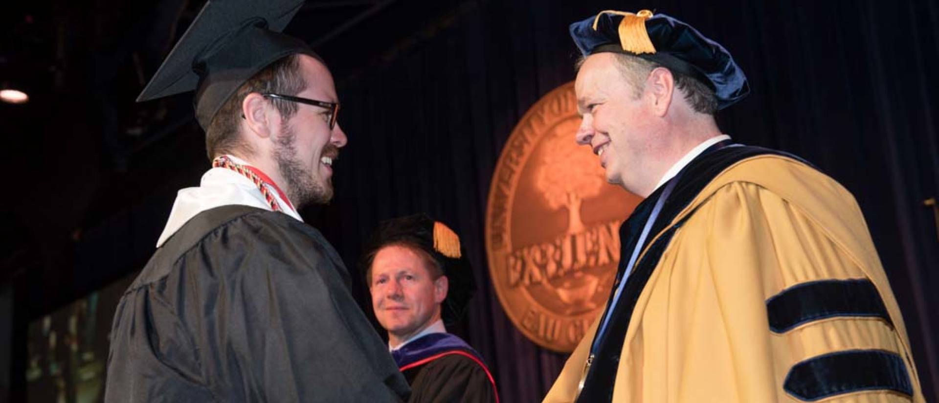 A Blugold shakes Chancellor James C. Schmidt's hand on stage during commencement.