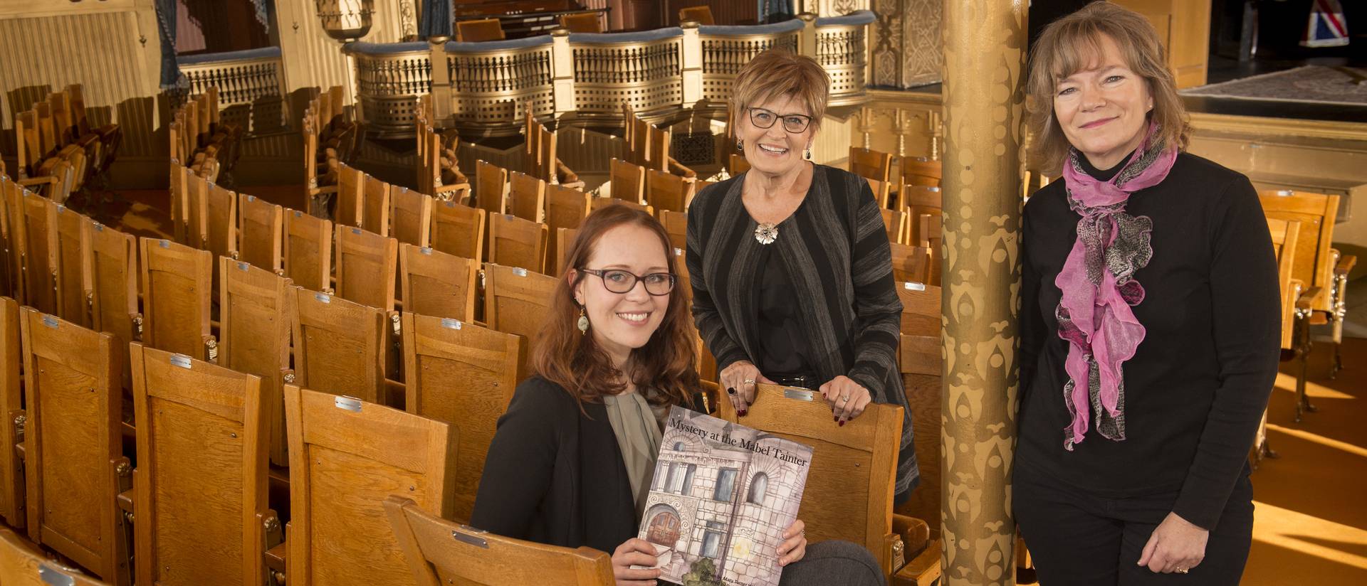 Mary Heimstead and Taylor Kysely pose with their book "Mystery at the Mabel Tainter" with another woman in the Mabel Tainter Center for the Arts in Menomonie, WI.