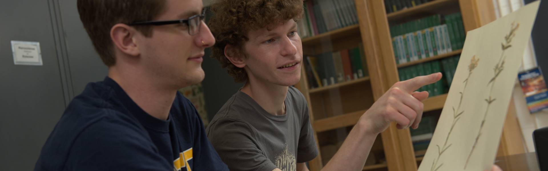 Two students observe a picture of flowers in a biology classroom.