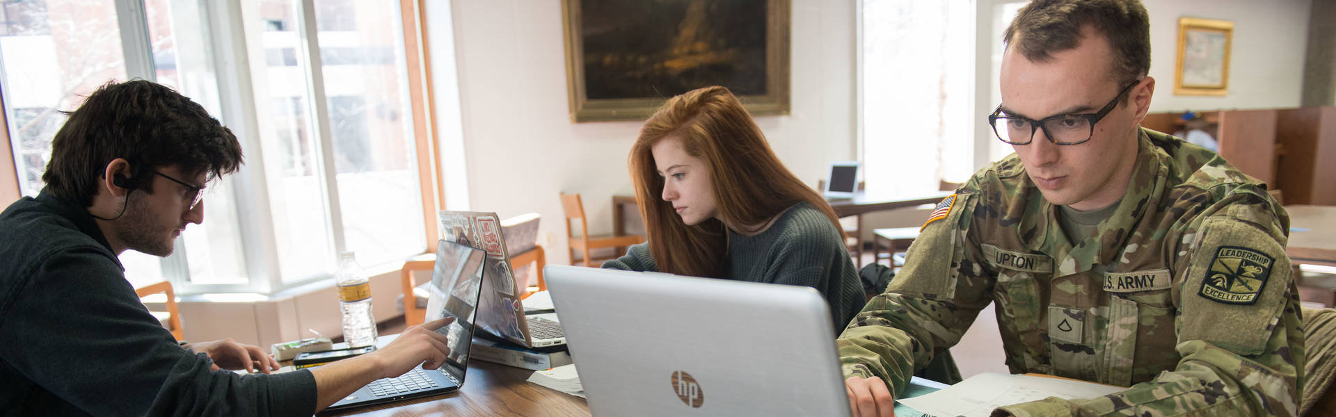 ROTC student in uniform and other students studying in the library