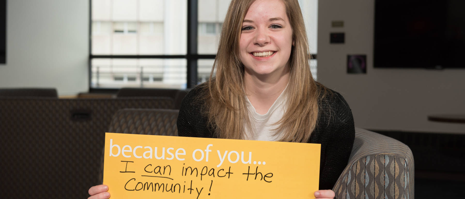 Girl holding sign that says: "Because of you, I can impact the community!"