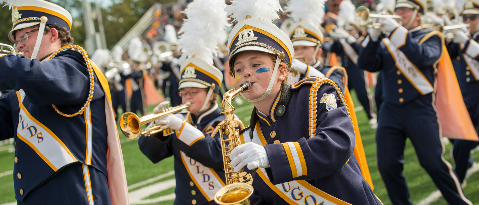 Student playing saxophone in marching band while dancing on football field