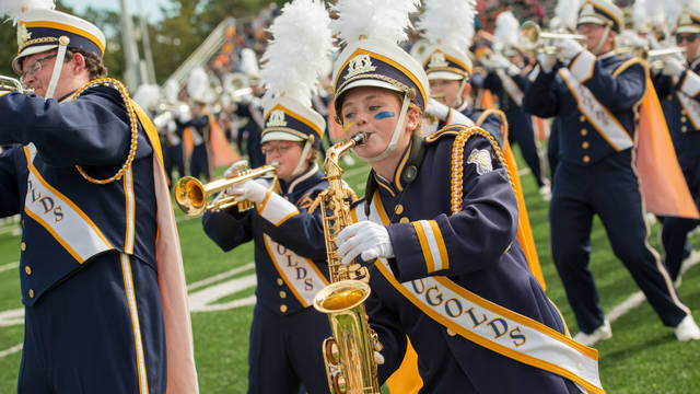 Student playing saxophone in marching band while dancing on football field