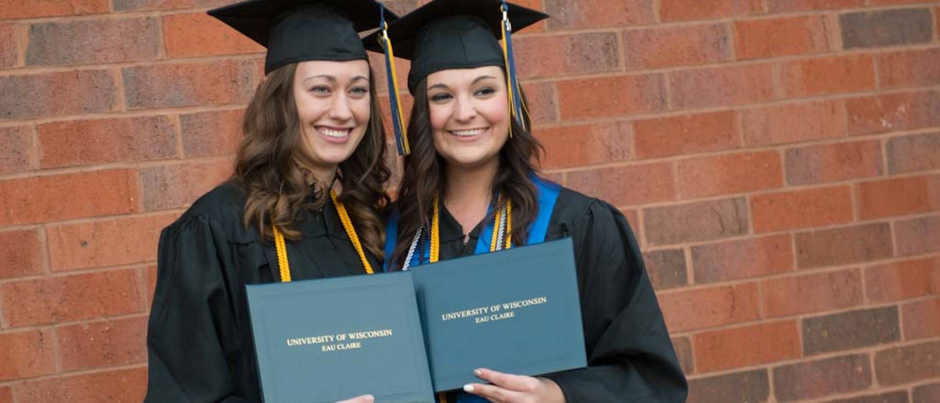 Two graduates holding their diplomas during the afternoon commencement.